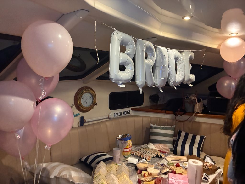 Hens party boat interior decorated with BRIDE balloon banner, pink balloons and grazing table on Gold Coast cruise